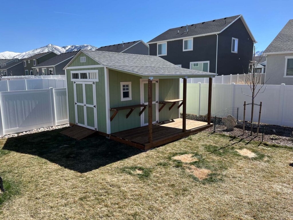 Custom-built garden shed in Utah with deck and awning featuring designer green paint and white trim by Solitude Custom Sheds.