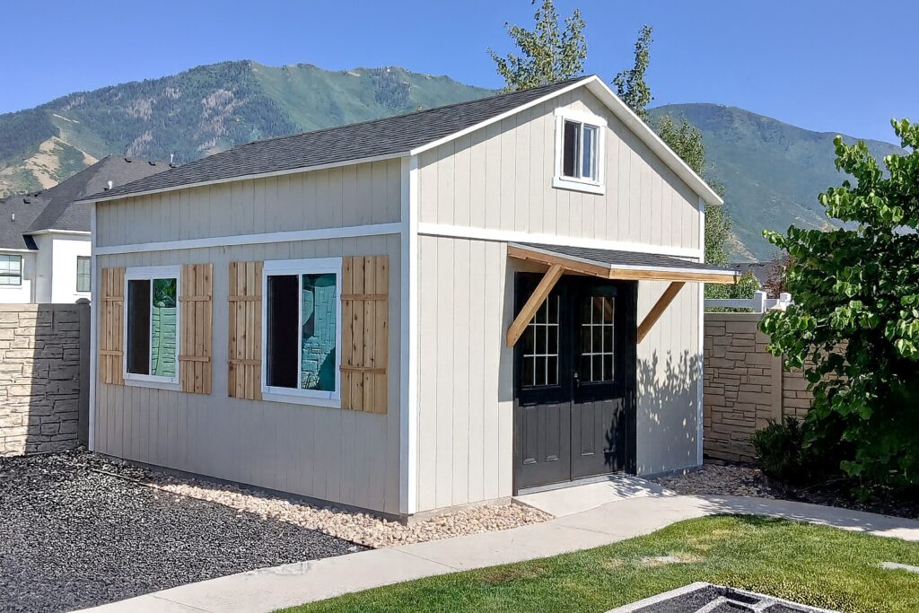 16x20 custom outdoor storage shed with 10' walls built by Solitude Custom Sheds in Mapleton, Utah; featuring a modern tan exterior, black French doors, awning across the front front, over-sized windows and premium craftsmanship for backyard storage or workshop use.