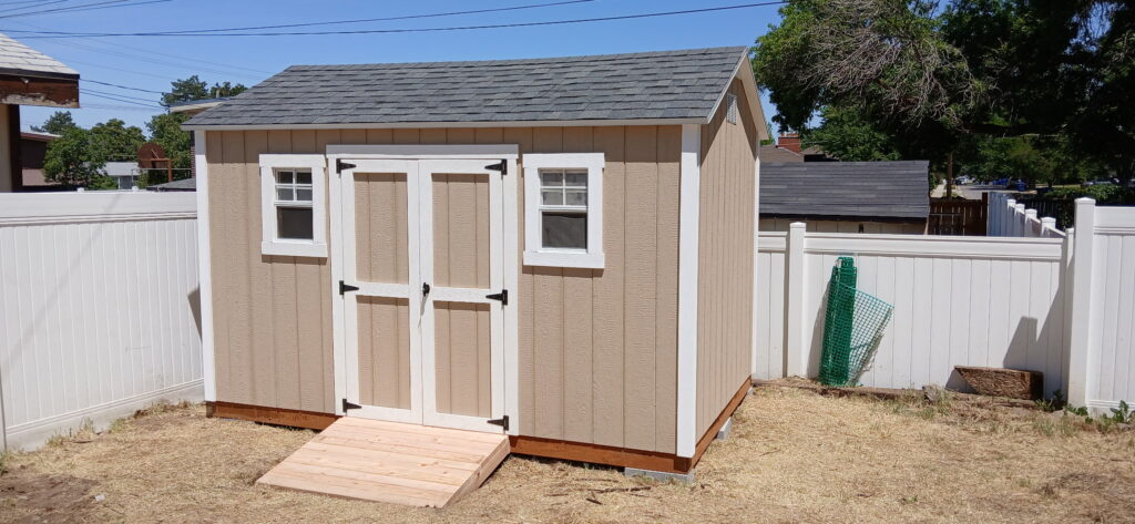 8x12 custom outdoor storage shed in Cottonwood Heights, Utah built by Solitude Custom Sheds featuring 5-foot double doors with windows, a custom-built wooden ramp, and durable tan siding with white trim.