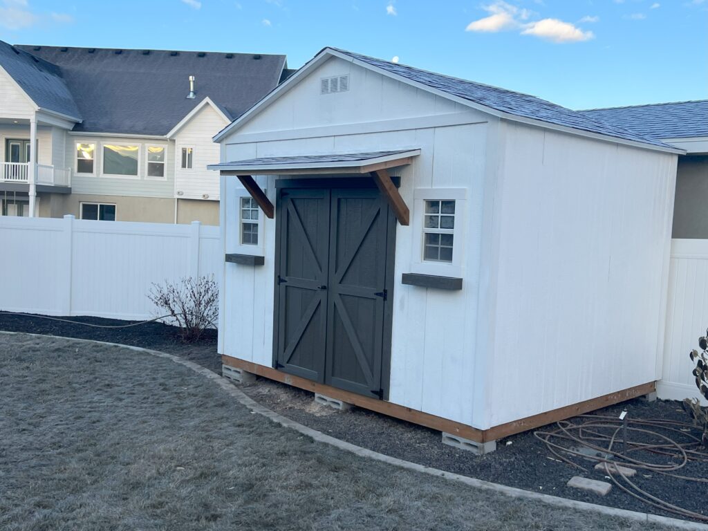 10x12 custom outdoor storage shed with 8-foot walls, gray double barn doors, wood awning, and decorative flower boxes built by Solitude Custom Sheds in Cottonwood Heights, Utah, serving Salt Lake County homeowners.