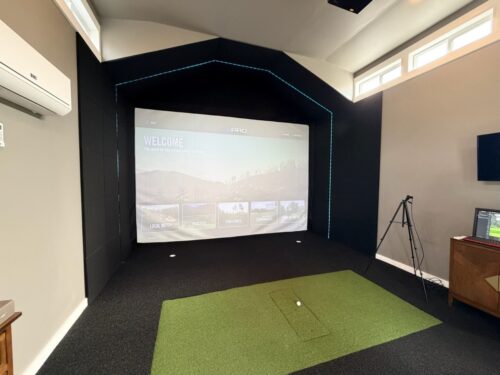 Interior of a 15x21 custom golf simulator studio built by Solitude Custom Sheds in Herriman, Utah featuring turf flooring, impact screen, and premium indoor golf setup