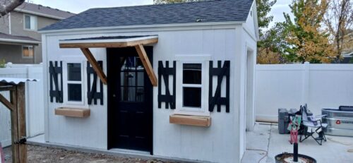 12x14 custom outdoor storage shed with black shutters, window boxes, and wood awning in Stansbury Park, Utah built by Solitude Custom Sheds