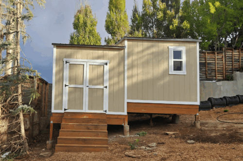 Split-level 10x18 custom outdoor storage shed in Salt Lake City, Utah with elevated foundation, double doors, and beige siding by Solitude Custom Sheds